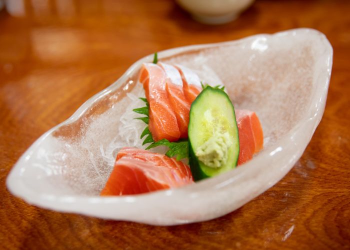 a textured glass bowl with slices of salmon sashimi, shredded daikon, and shiso