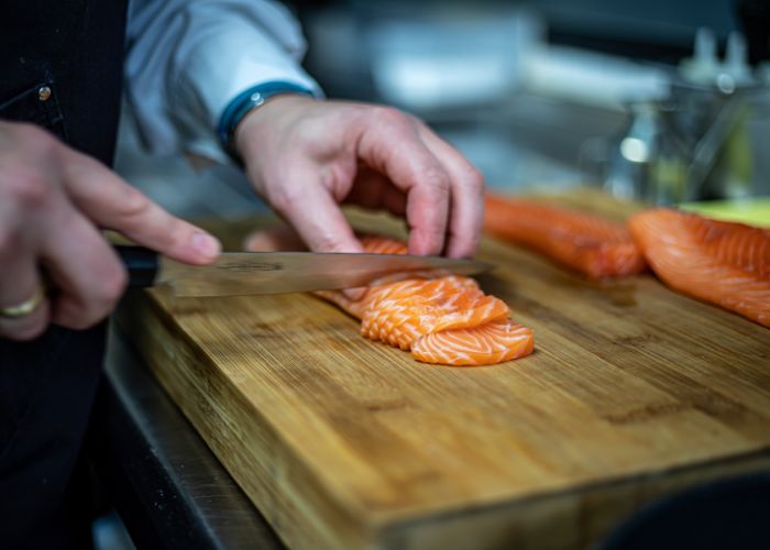 A sushi chef's hands carefully cut into well marbled salmon sashimi using a yanagiba knife