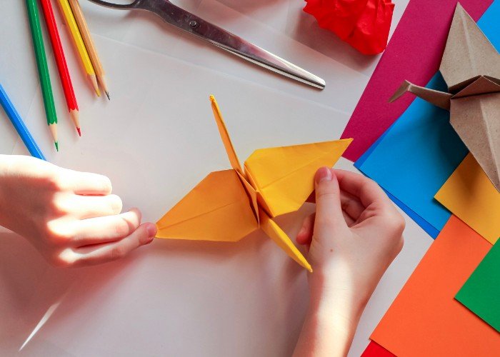 A child's hands work on an origami crane