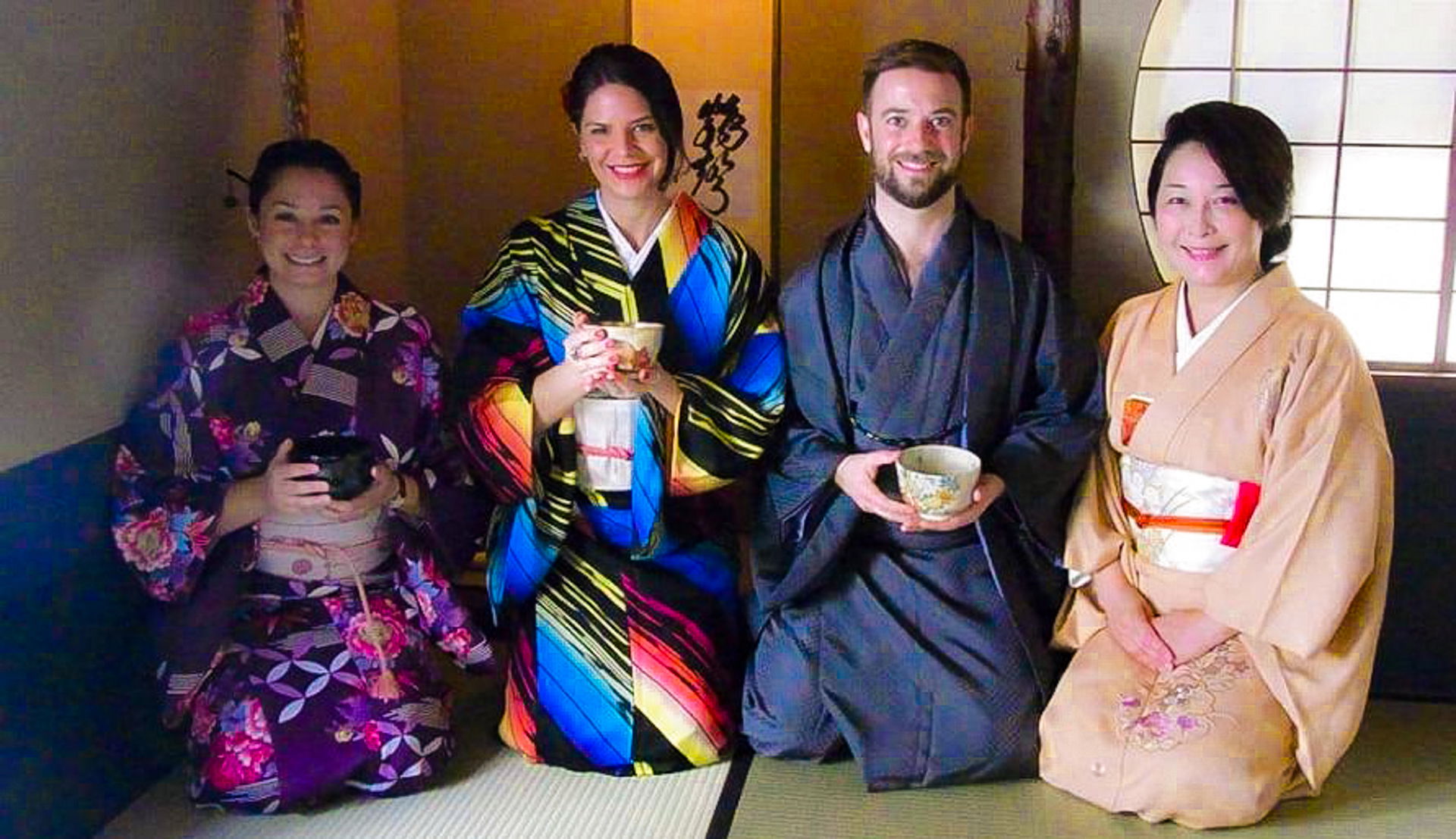 A tea ceremony experience in Asakusa. Guests are wearing kimono, holding matcha tea and smiling.