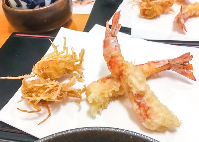 Shrimp tempura, with both the heads and bodies of two shrimp, rest on a plate 