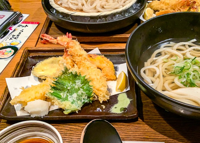 Various tempura next to a bowl of udon