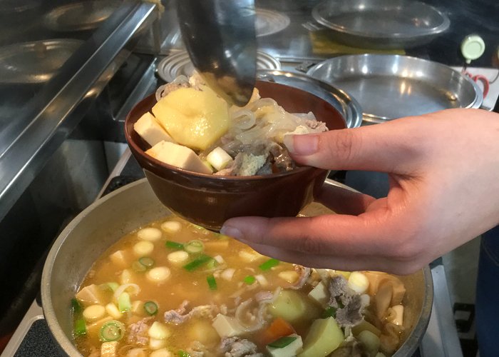A woman's hand holds a bowl of nabe over a pot of nabe