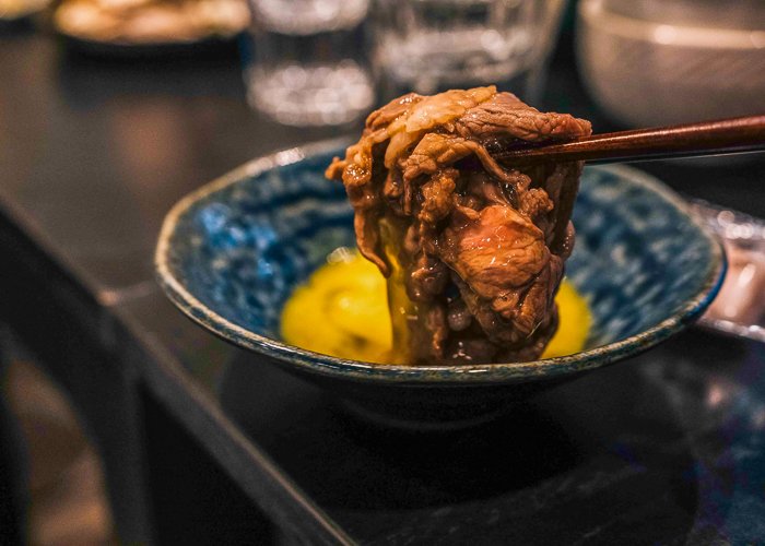 Sukiyaki meat held in chopsticks dipped into raw egg