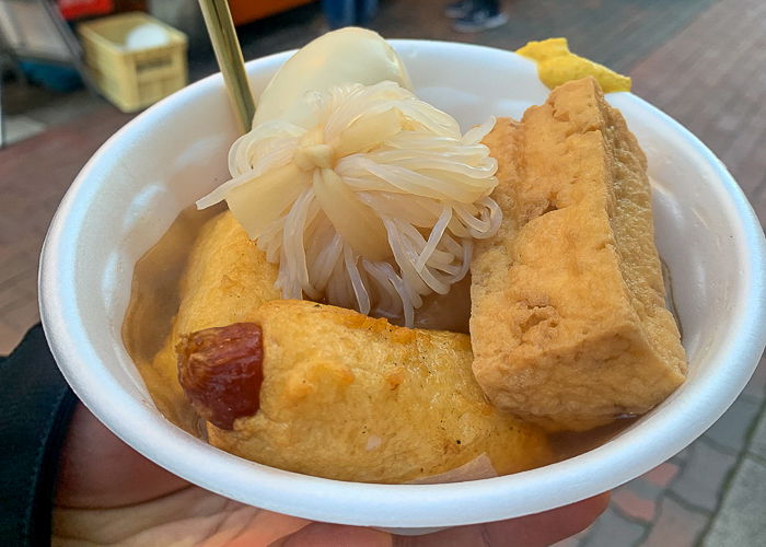 A man holds a bowl of oden 