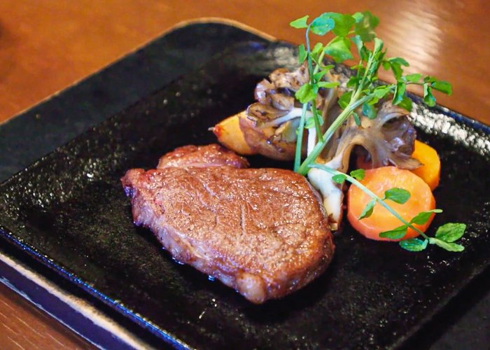 A black plate with wagyu beef and vegetables on it
