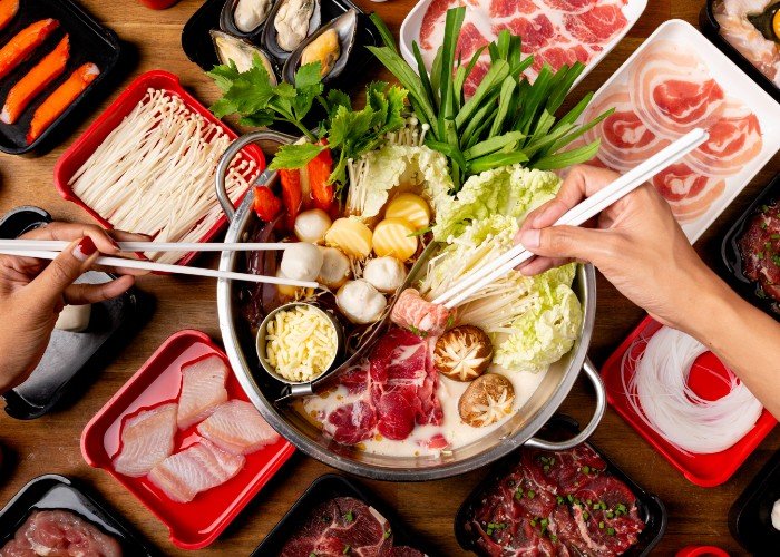 two hands holding chopsticks pick up ingredients from a Japanese hot pot
