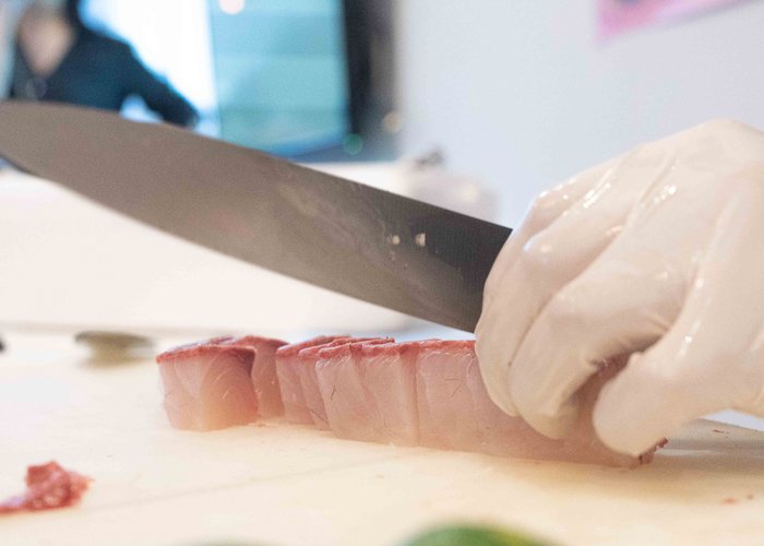 A  gloved hand holding a knife cutting sashimi
