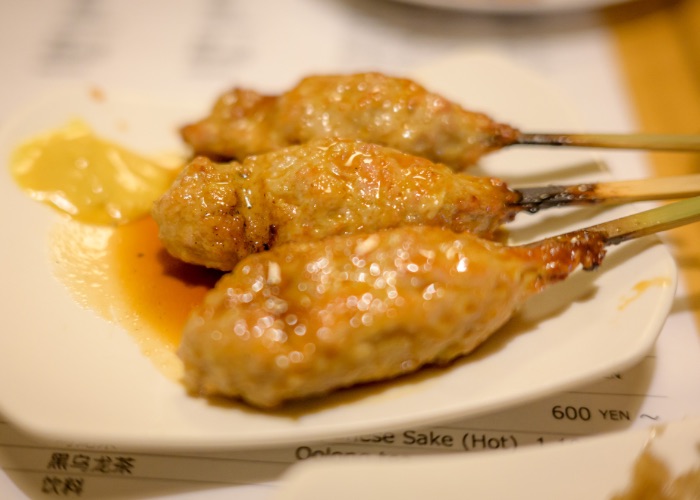 Three yakitori Tsukune skewers on a plate with mustard.