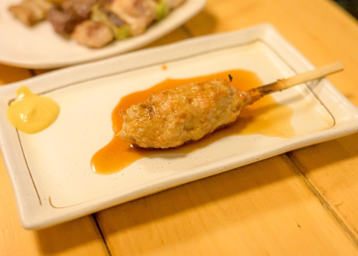 A single chicken meatball yakitori skewer on a plate with mustard.
