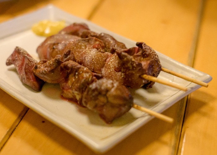 Three skewers of chicken liver yakitori on a plate with mustard.