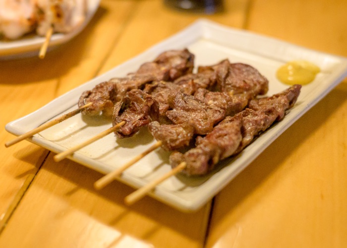 Four chicken heart yakitori skewers on a plate with mustard.
