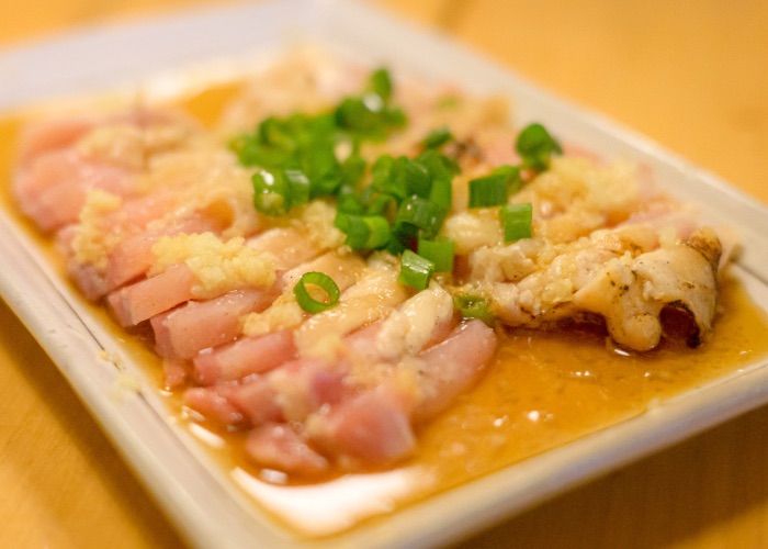 A plate of raw chicken sashimi topped with ginger and spring onions.