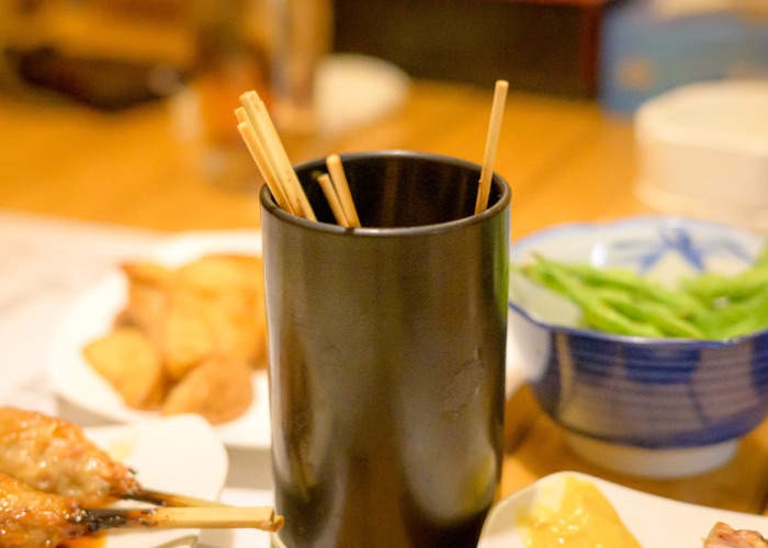 A black cup containing used yakitori skewers.