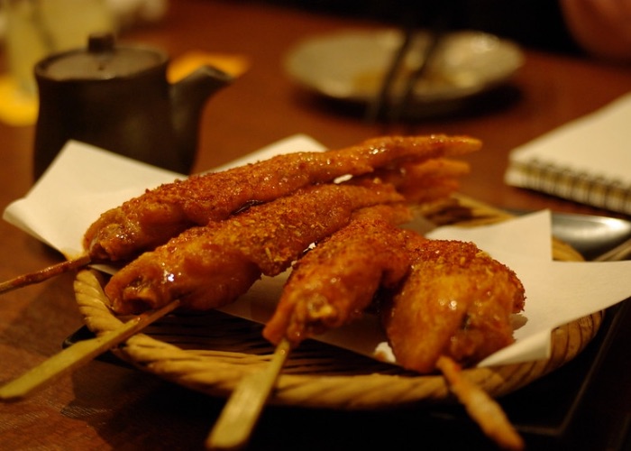 Four chicken wing yakitori skewers in a wicker basket.