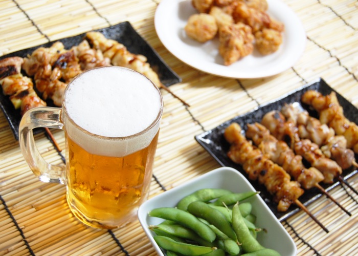 A glass of beer surrounded by plates of edamame and yakitori.