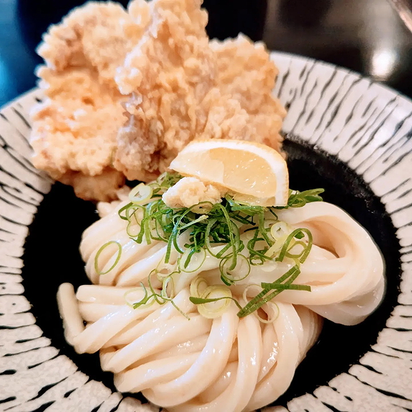 Delicious udon noodles with crispy tempura and lemon wedge