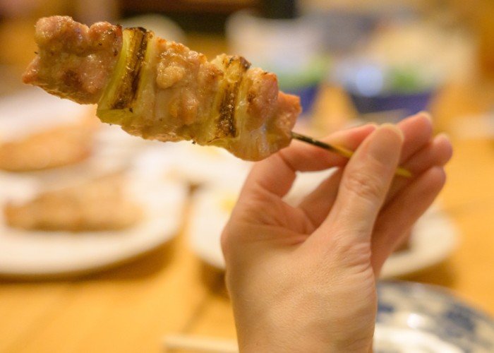 A women's hand holds a yakitori chicken skewer 