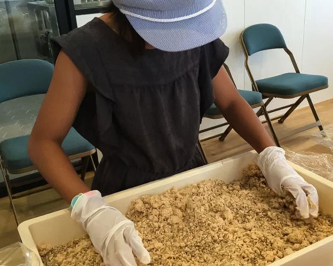 Someone wearing white gloves working with a tray of miso paste.