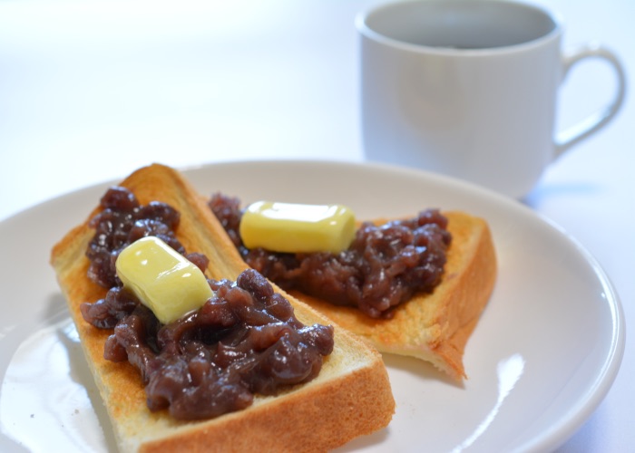 Two slices of toast topped with red bean paste and butter, a cup of coffee in the background.