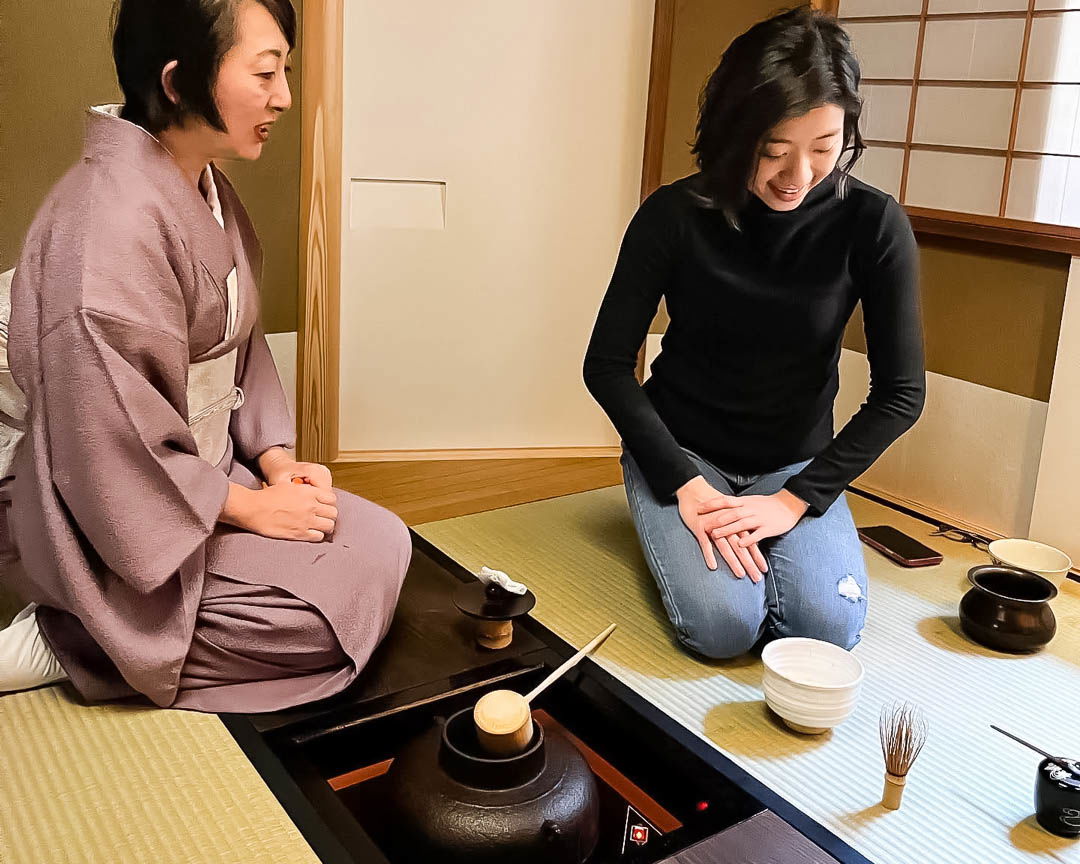 An expert host wearing a traditional kimono and guiding a guest on how to make matcha.