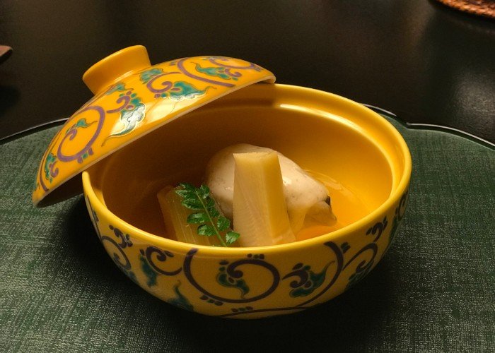 A dish from a Japanese kaiseki style dinner served in bright yellow ornate bowl.