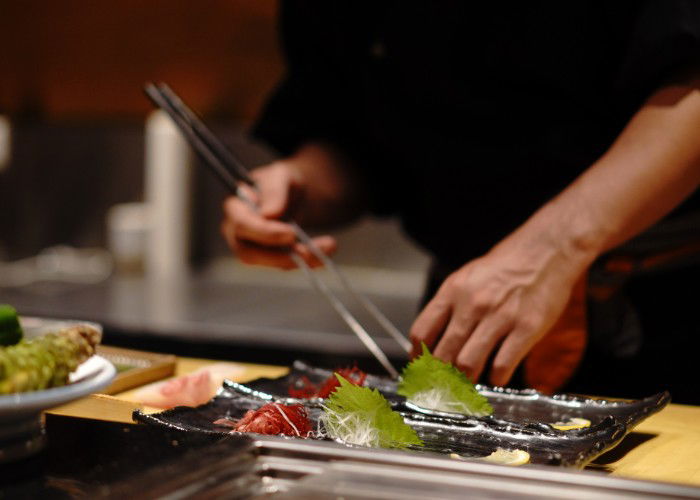 Close-up hand of Japanese chef making sushi, decorating cucumber on black background. The chef decorates cucumber sushi before serving.