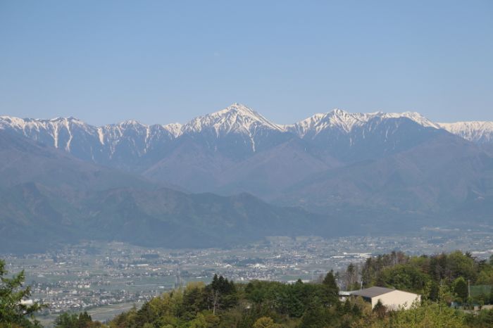 A sweeping view of the Japanese Alps with Matsumoto spread out along the valley and a small mountain in the foreground