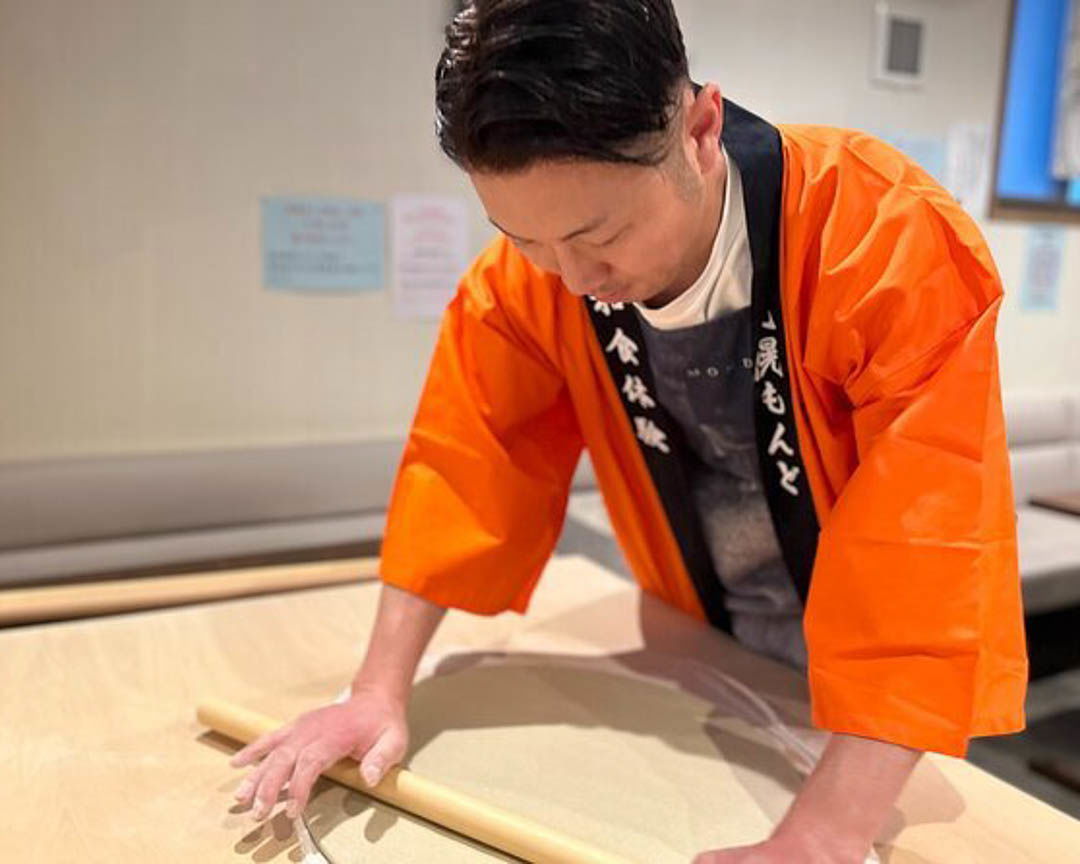 A man using a rolling pin to flatten soba dough during a cooking class in Sapporo