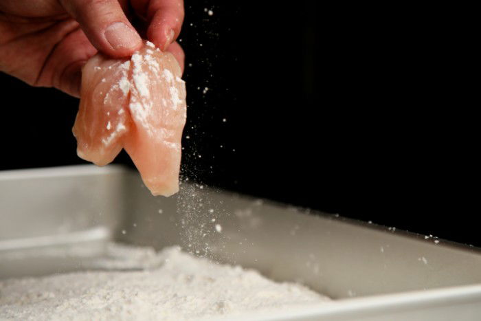 a hand dipping a piece of chicken into flour to make karaage