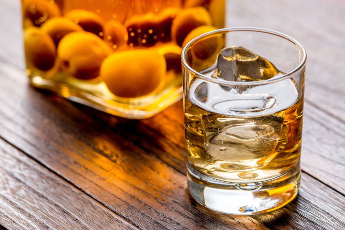 A glass of umeshu with ice, and a jar of umeshu nearby