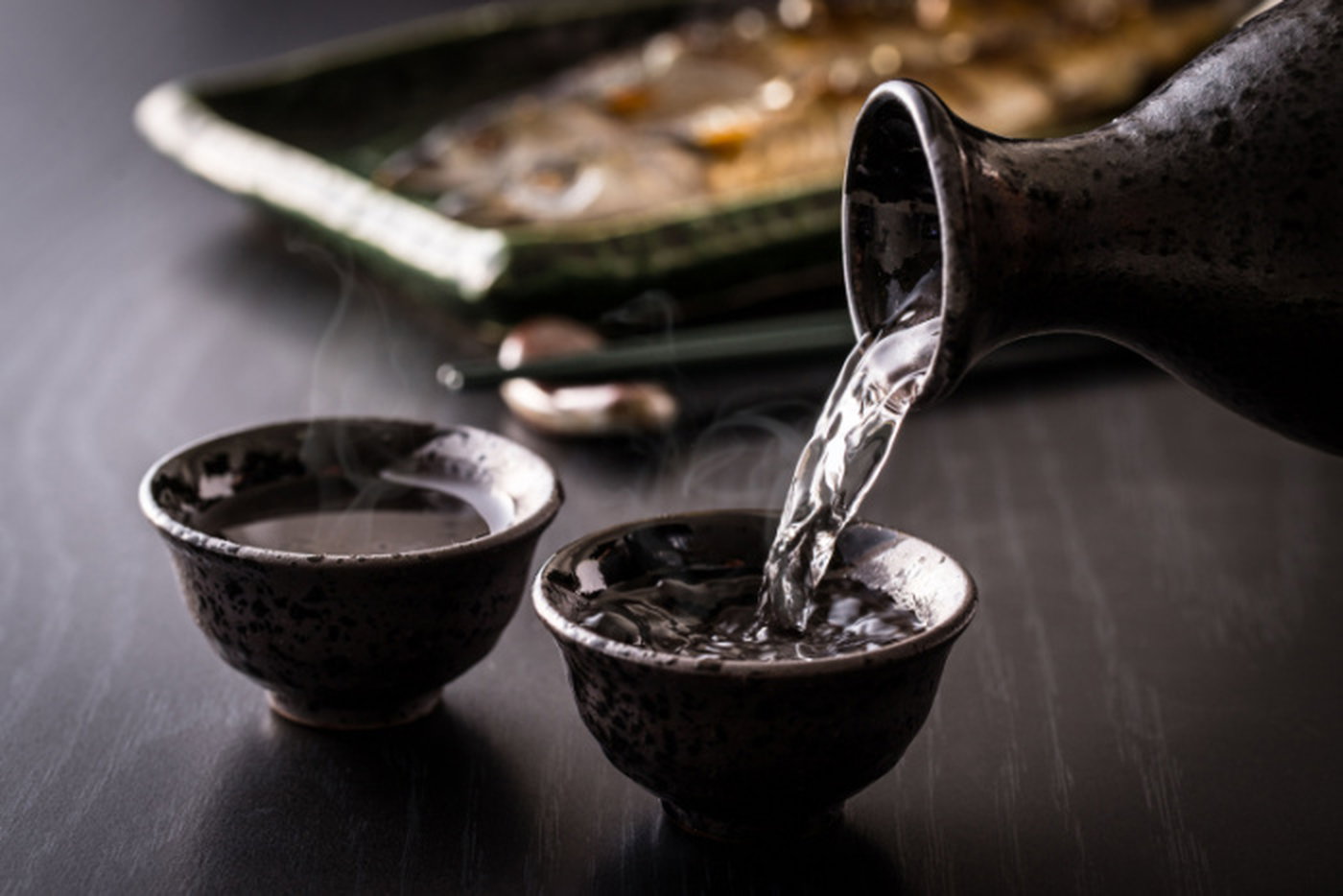 Hot Japanese sake being poured into two small black cups