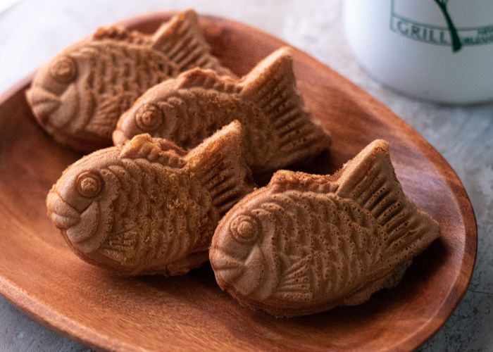 Four taiyaki, a Japanese dessert shaped like a fish, on a wooden plate