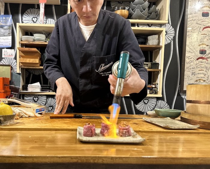 Sushi Chef Saisho flame-grilling a dish of sashimi
