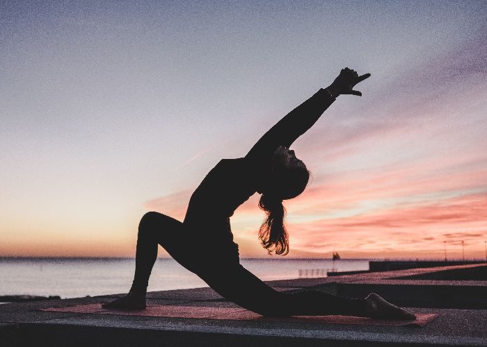 A girl doing a yoga stretch pointing at the sky at sunset