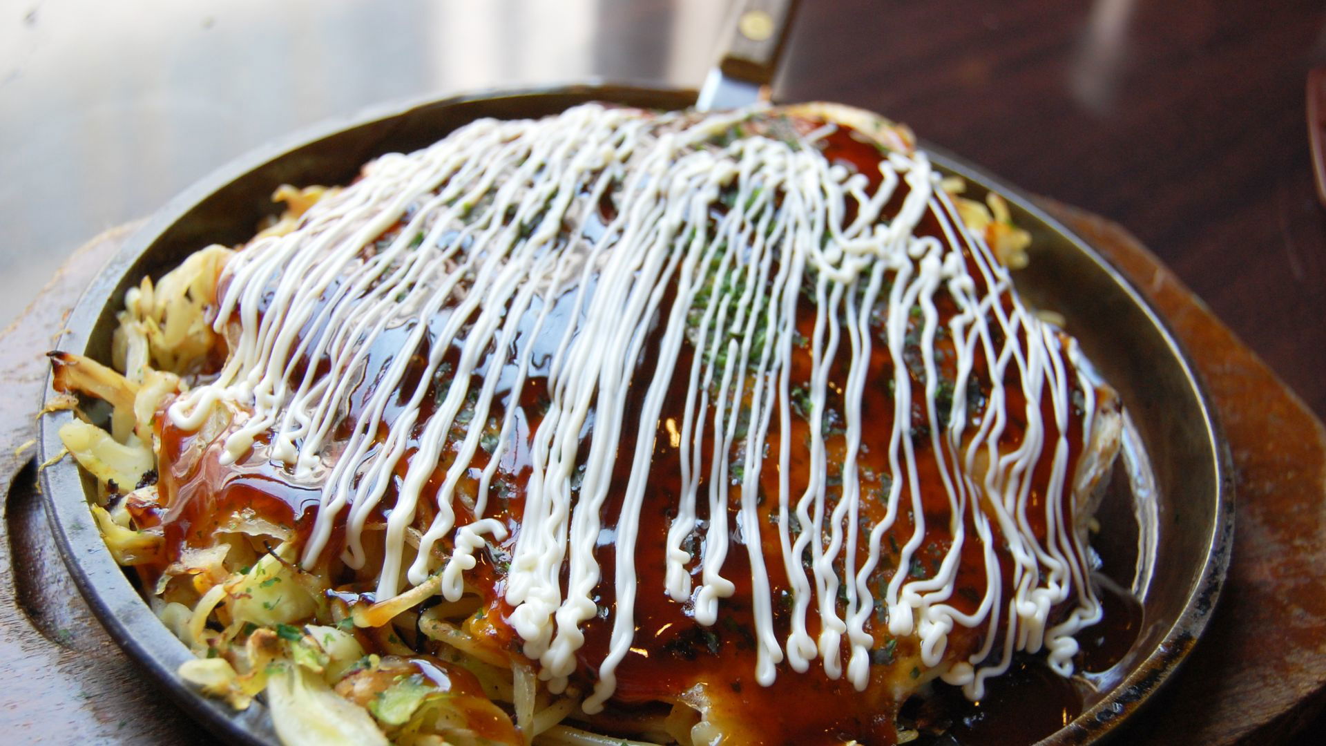 Savory Japanese okonomiyaki topped with mayo and sauce on a skillet