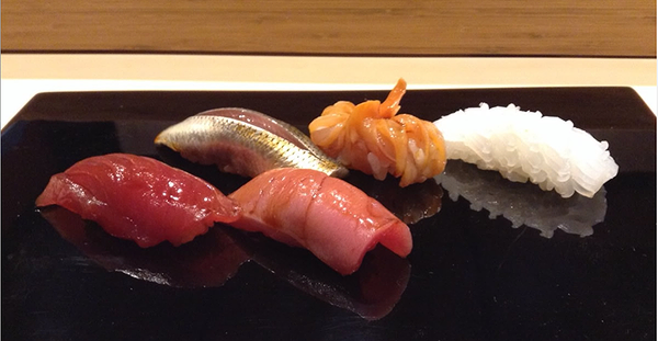 Assorted sushi nigiri on a black platter in a modern restaurant setting.