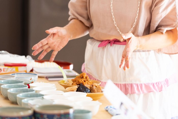 A Japanese cooking class instructor holds her hands over various bowls and ingredients