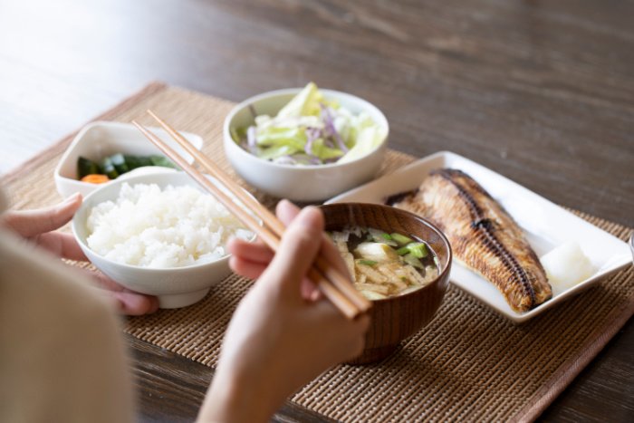 A person eating a healthy Japanese breakfast set of rice, grilled fish, vegetables and miso soup