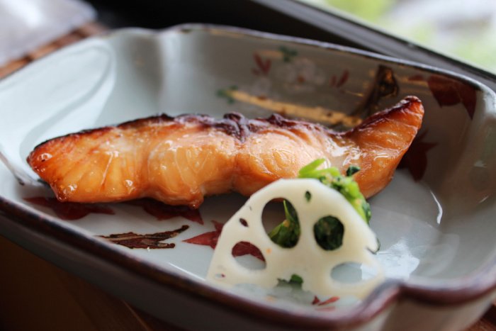 A piece of grilled salmon and lotus root in a Japanese traditional meal