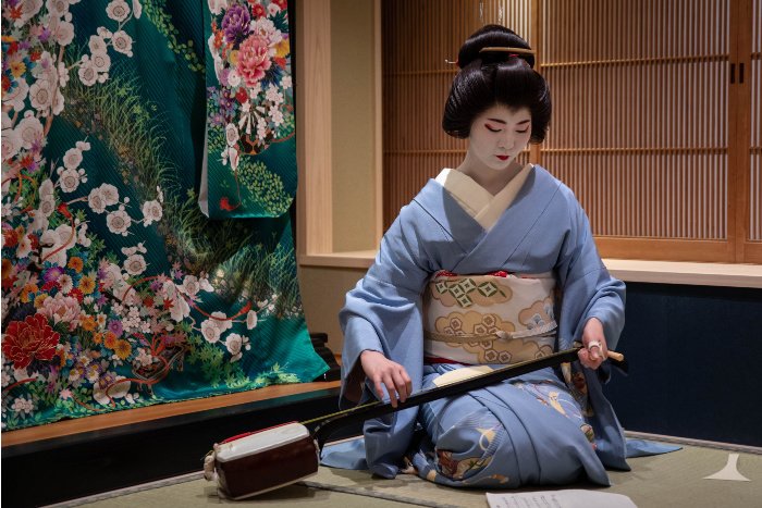 A geisha tunes her instrument in a tatami room