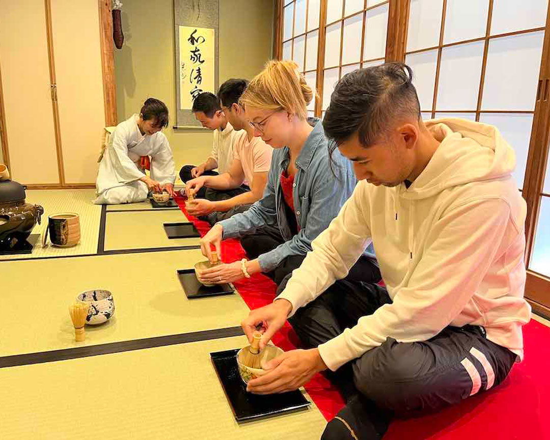 Guests in a traditional tatami room, whisking green tea at a Japanese tea ceremony in Osaka.