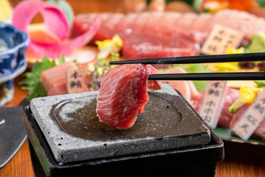 Chopsticks holding a piece of Takumi Gotanda, ready for dipping.