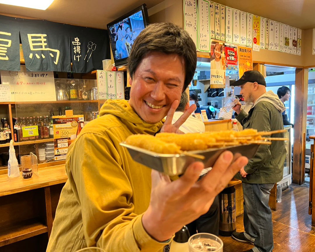 Someone throwing a peace sign while holding deep-fried izakaya foods.