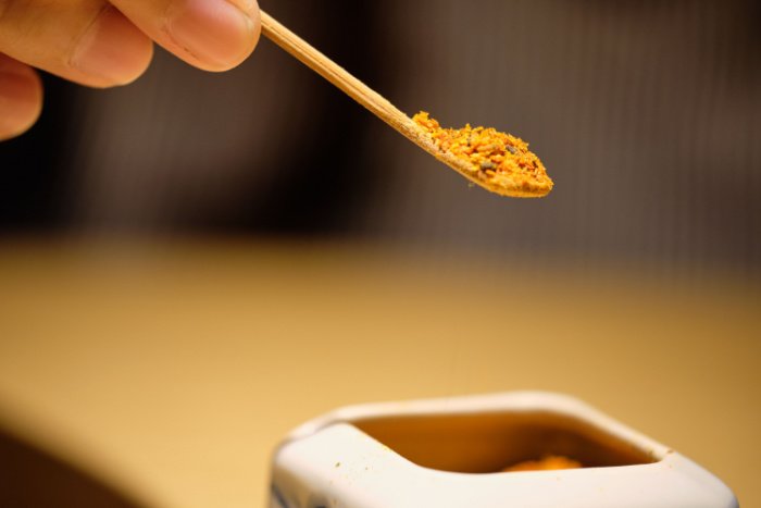 A close-up of a hand holding a teaspoon of Japanese togarashi pepper