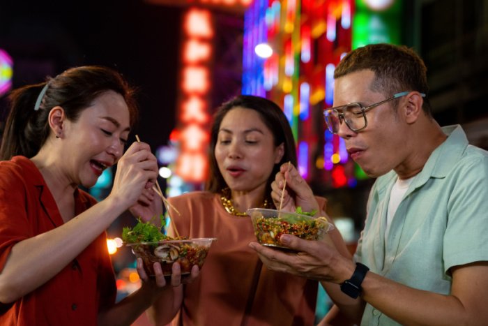Three people eating spicy food on a night street 