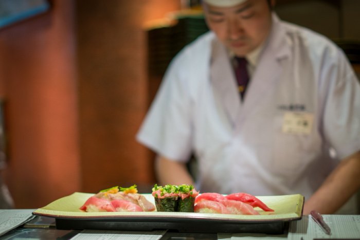 A sushi chef serves a platter of tuna nigiri sushi