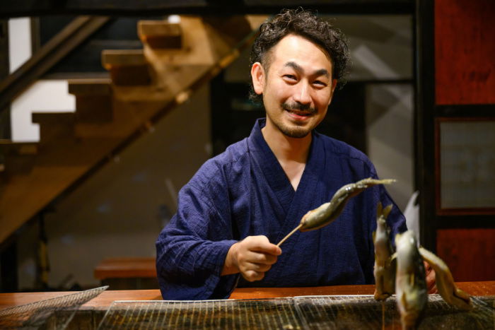 Chef grilling skewered fish in a traditional setting