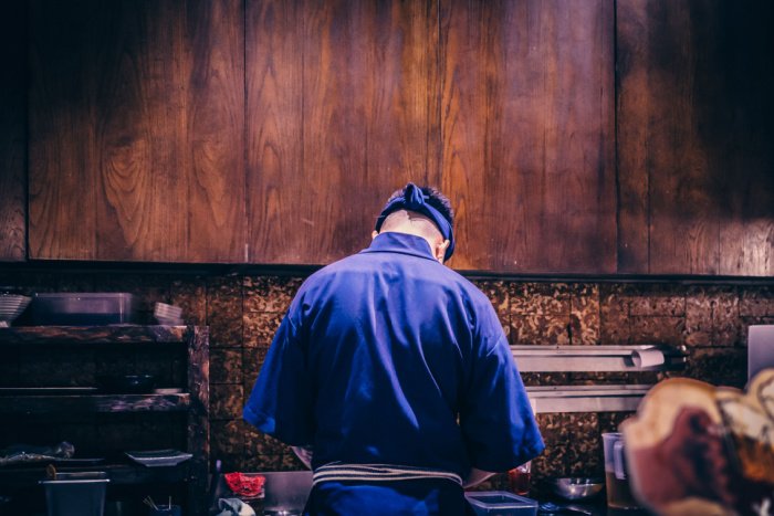 A robatayaki chef in blue samue, with his back turned to the camera
