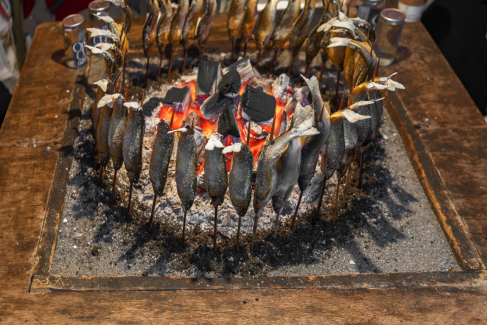 A circle of skewered fish being cooked around a robata grill